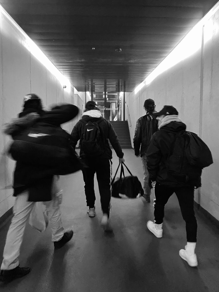 Four men walking through a concrete passageway, photographed in black and white